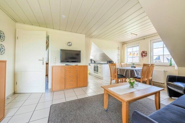 A spacious living area with a wooden table, a sofa, and a TV in the background.