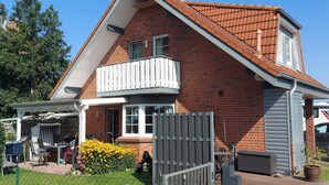A two-story house with a brick exterior, a balcony, and a covered patio area. - Ferienwohnung im OG in Friedrichkoog-Spitze (Friedrichskoog-Spitze)