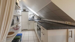 A narrow kitchen with white cabinets, a black countertop, and a microwave. There are shelves with kitchen items and a window above the sink. - Ferienwohnung im OG in Friedrichkoog-Spitze (Friedrichskoog-Spitze)