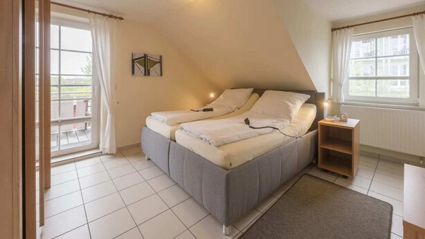 A bedroom with a bed, a nightstand, a window, and a door. - Ferienwohnung im OG in Friedrichkoog-Spitze (Friedrichskoog-Spitze)