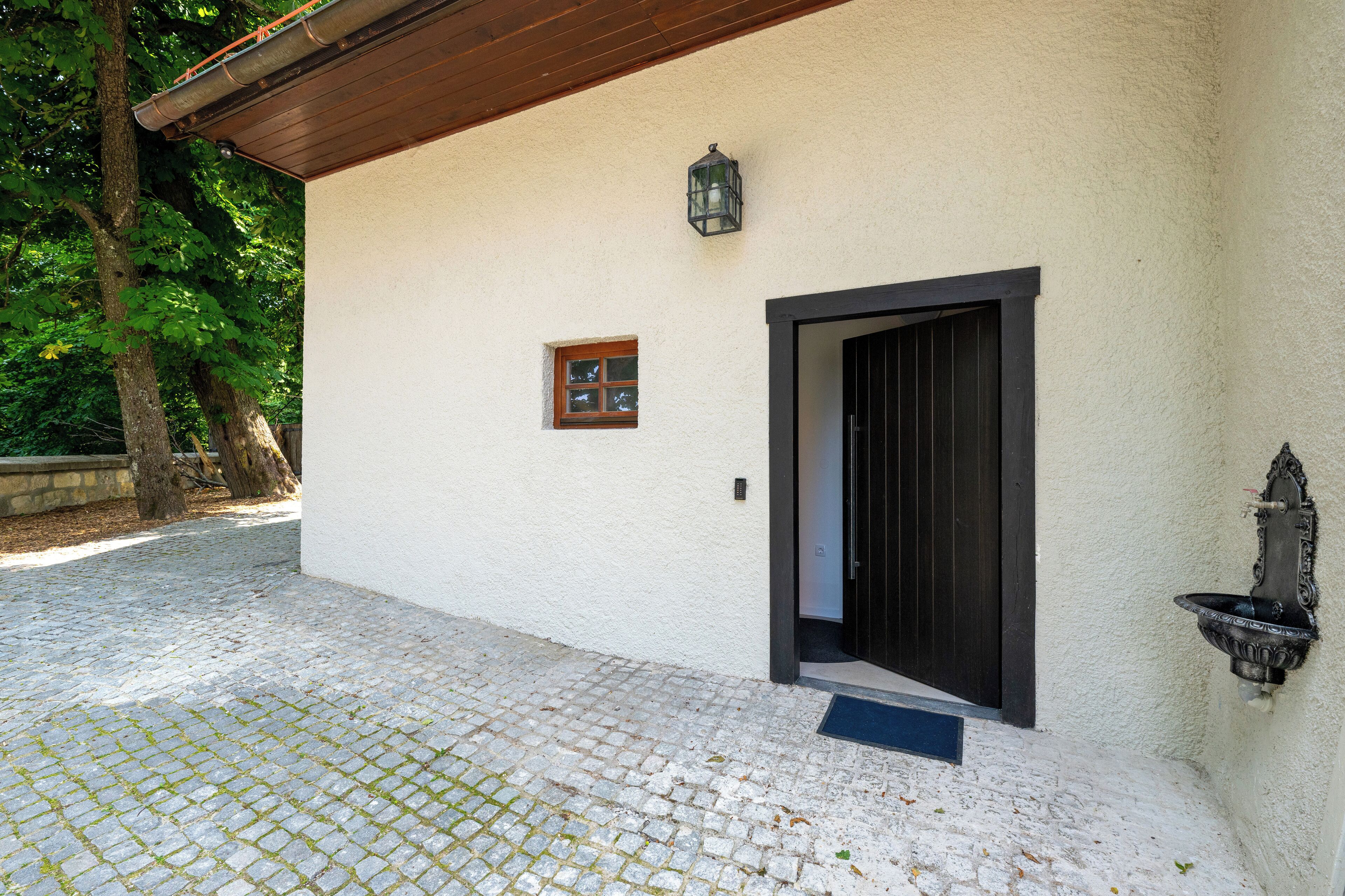 A building with a white exterior, a black door, a small window, and a wall-mounted light fixture.