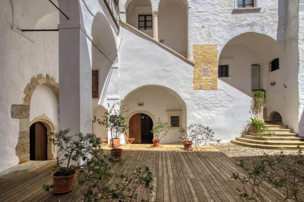 Un patio con paredes blancas, arcos, plantas en macetas y suelo de madera.