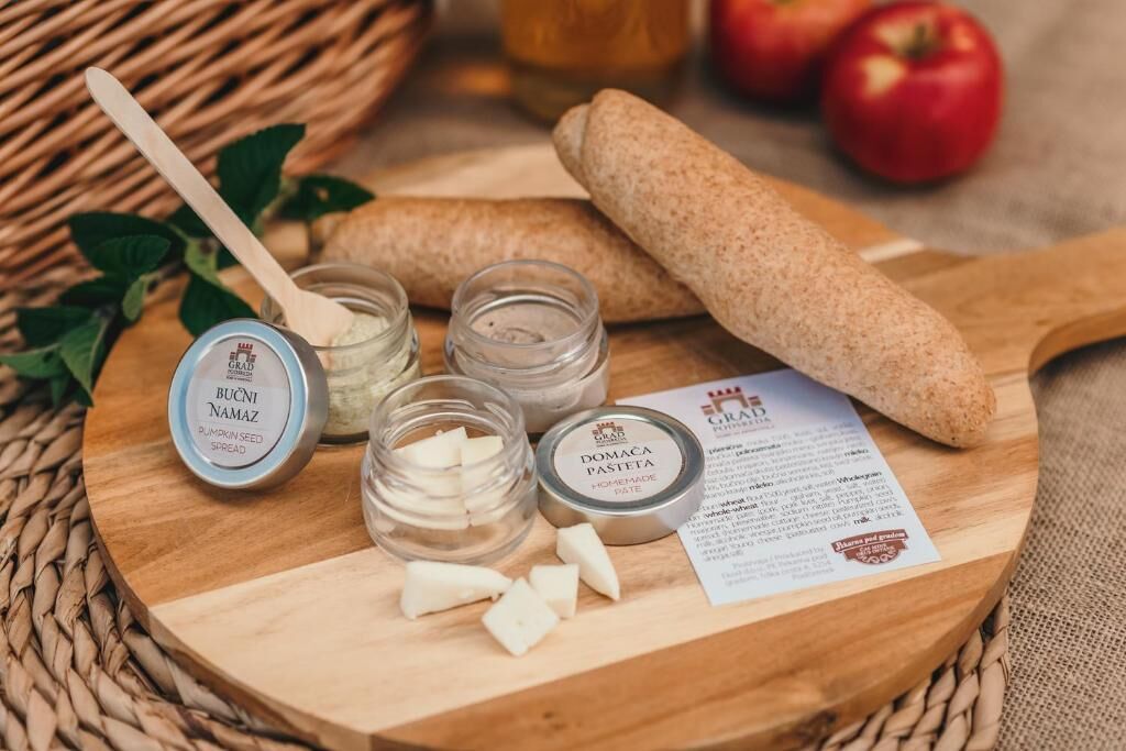 Una tabla de madera con botes de crema de semillas de calabaza y pasté casero, una hogaza de pan y un menú.