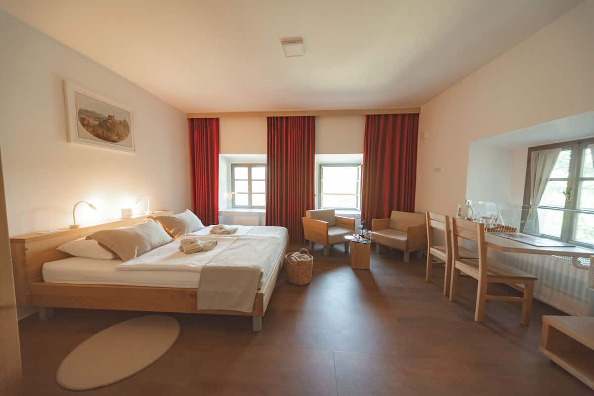 Habitación de hotel con dos camas, un escritorio y una silla. Hay ventanas con cortinas, un cuadro en la pared y un radiador.