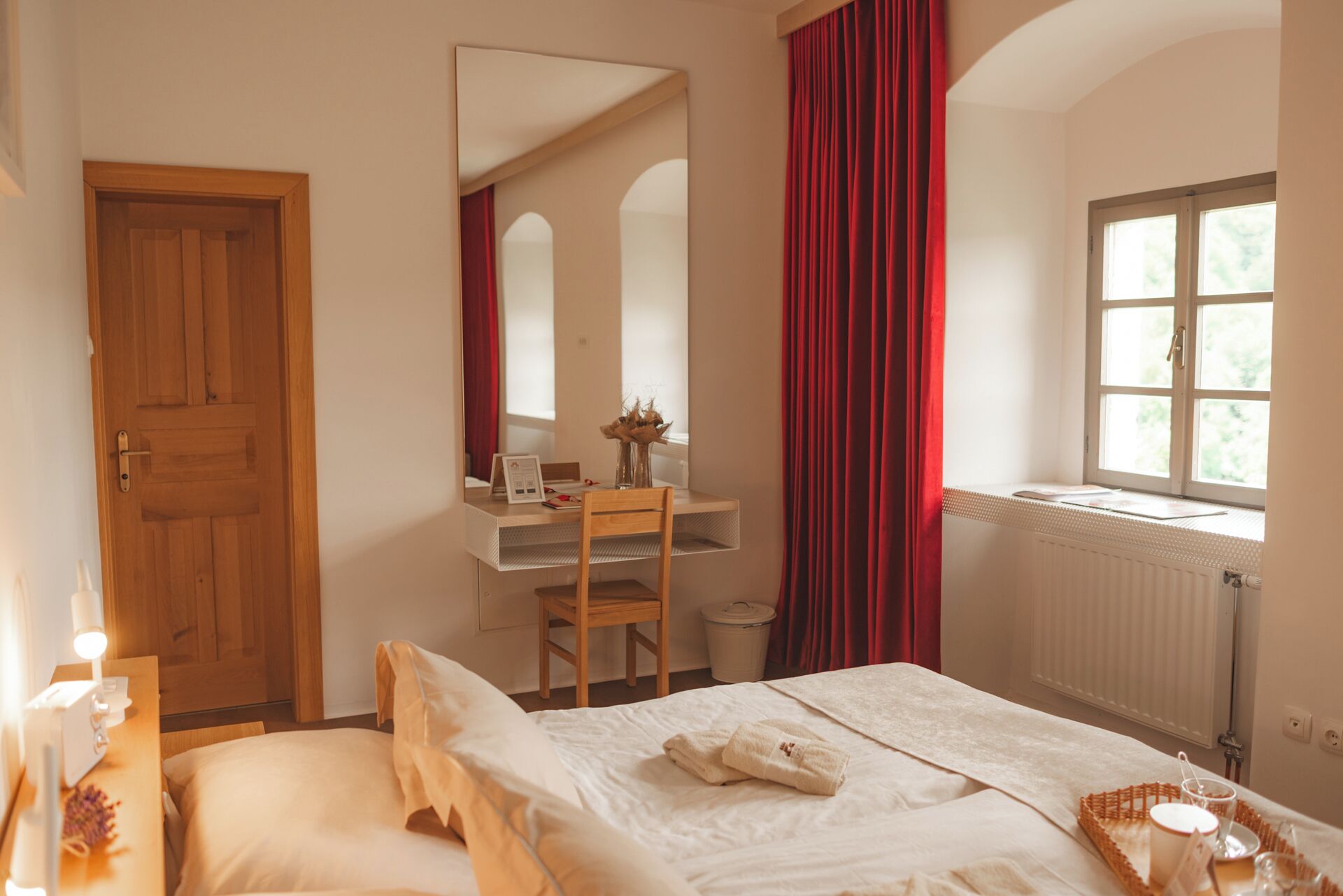 A bedroom with a bed, a desk, a mirror, a window, and a radiator.