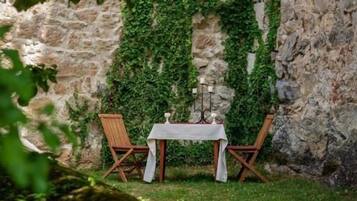 A stone wall with ivy, a table with a white tablecloth, two wooden chairs, and candle holders.
