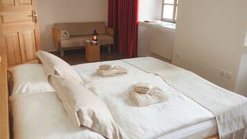 A neatly made bed with white linens and towels, a wooden wardrobe, a sofa, and a window with red curtains.