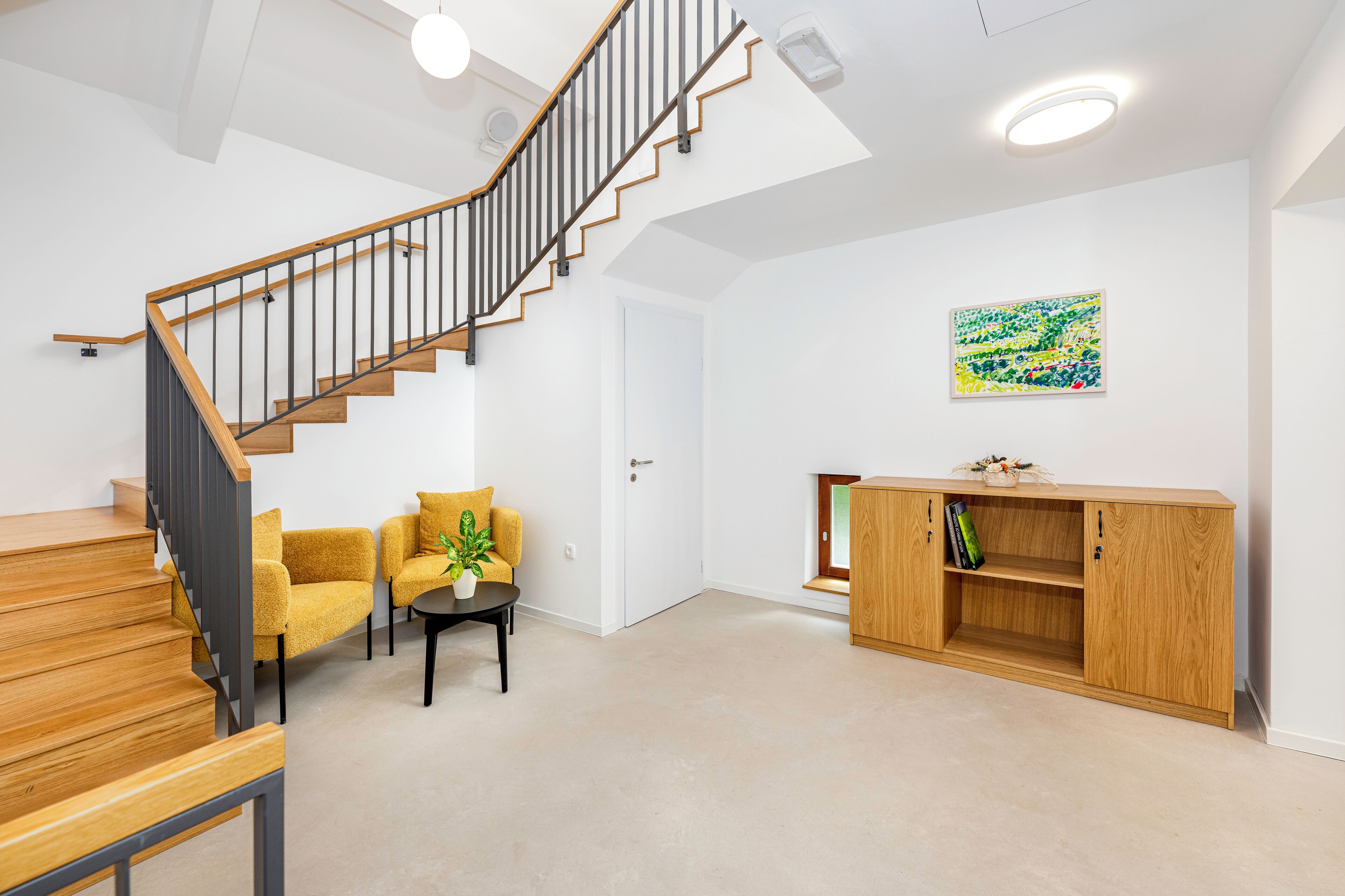Uma sala de estar moderna com escada de madeira, um conjunto de sofás, uma pequena mesa com uma planta e um armário de madeira.
