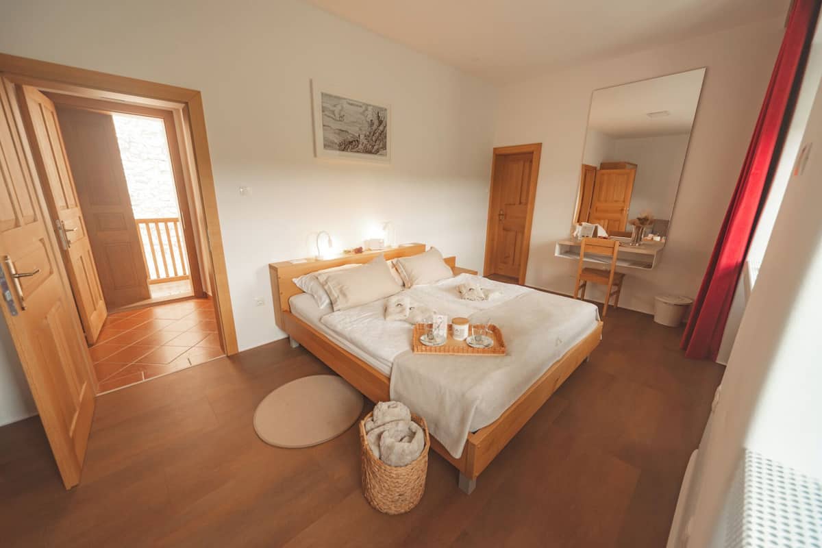 Un dormitorio con una cama de madera, una mesita de noche con lámpara, una alfombra redonda pequeña y una cesta de toallas.