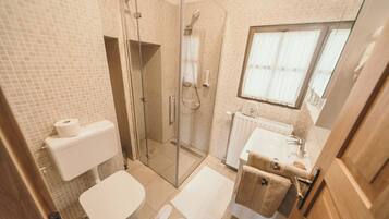 Un baño con ducha de vidrio, inodoro, lavabo y ventana.