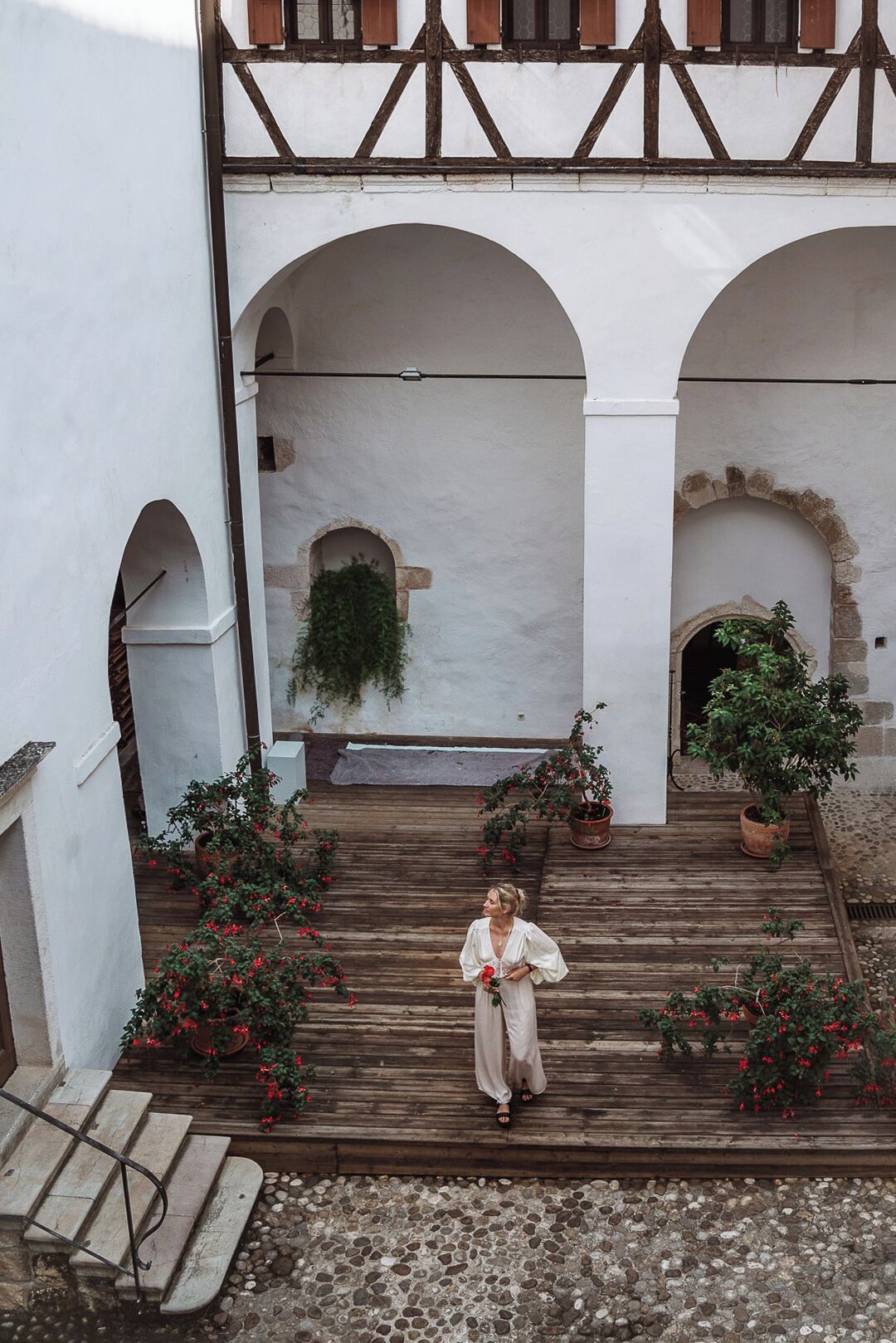 A courtyard with a wooden staircase leading to an upper level, surrounded by white walls and arches.