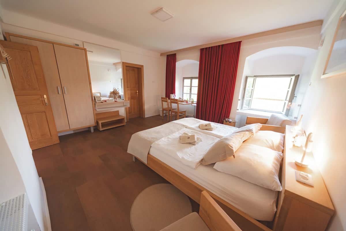 Una habitación de hotel con una cama grande, un escritorio, una silla, un armario y una ventana con cortinas.