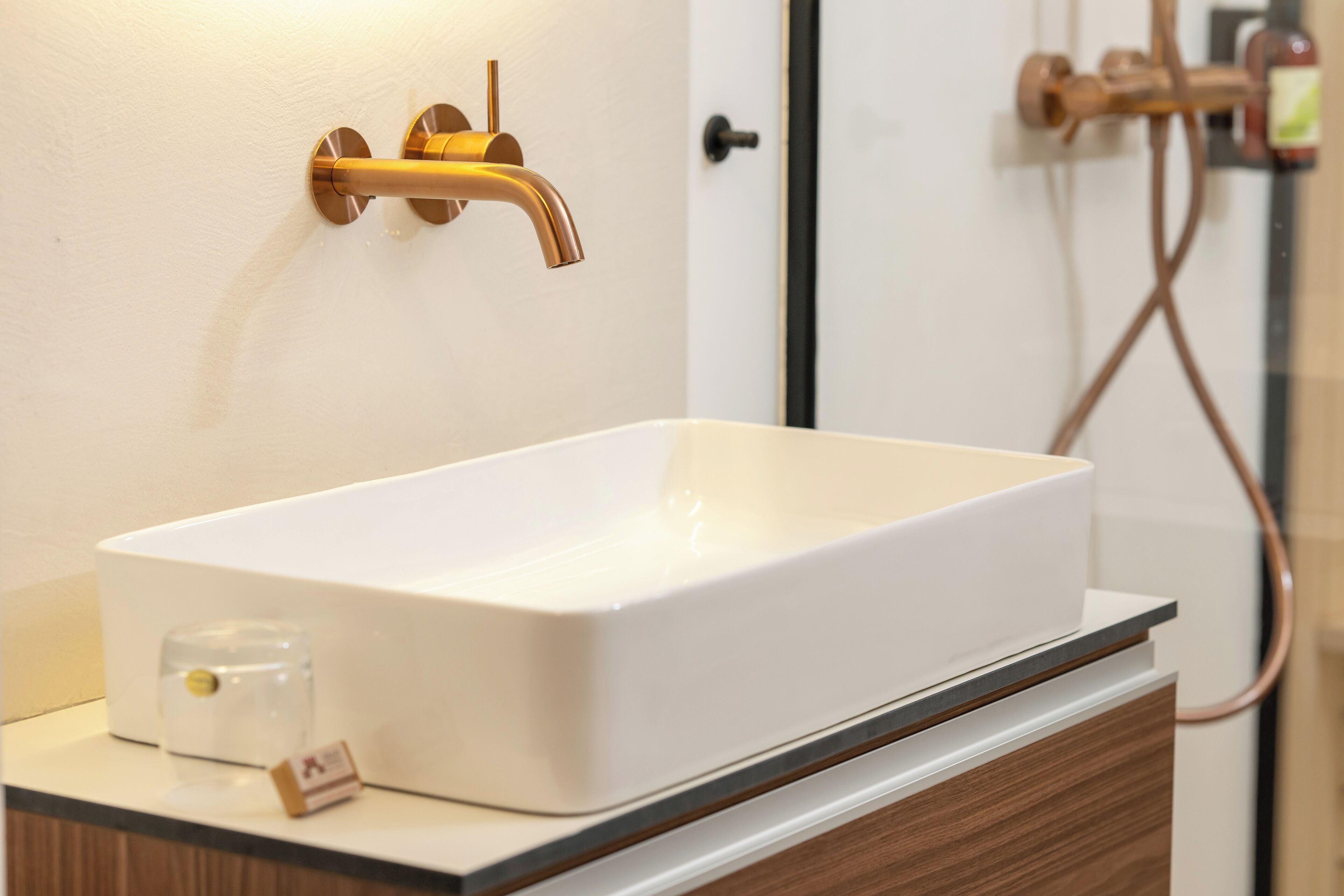 Une salle de bain avec un lavabo blanc, un robinet doré et un distributeur de savon en verre.