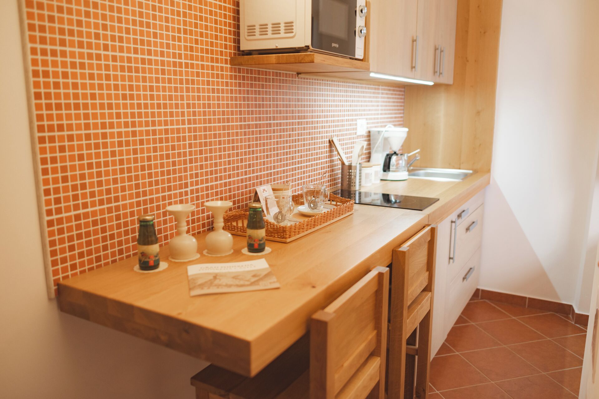 A kitchen with a wooden countertop, a microwave, a sink, and a tiled backsplash.