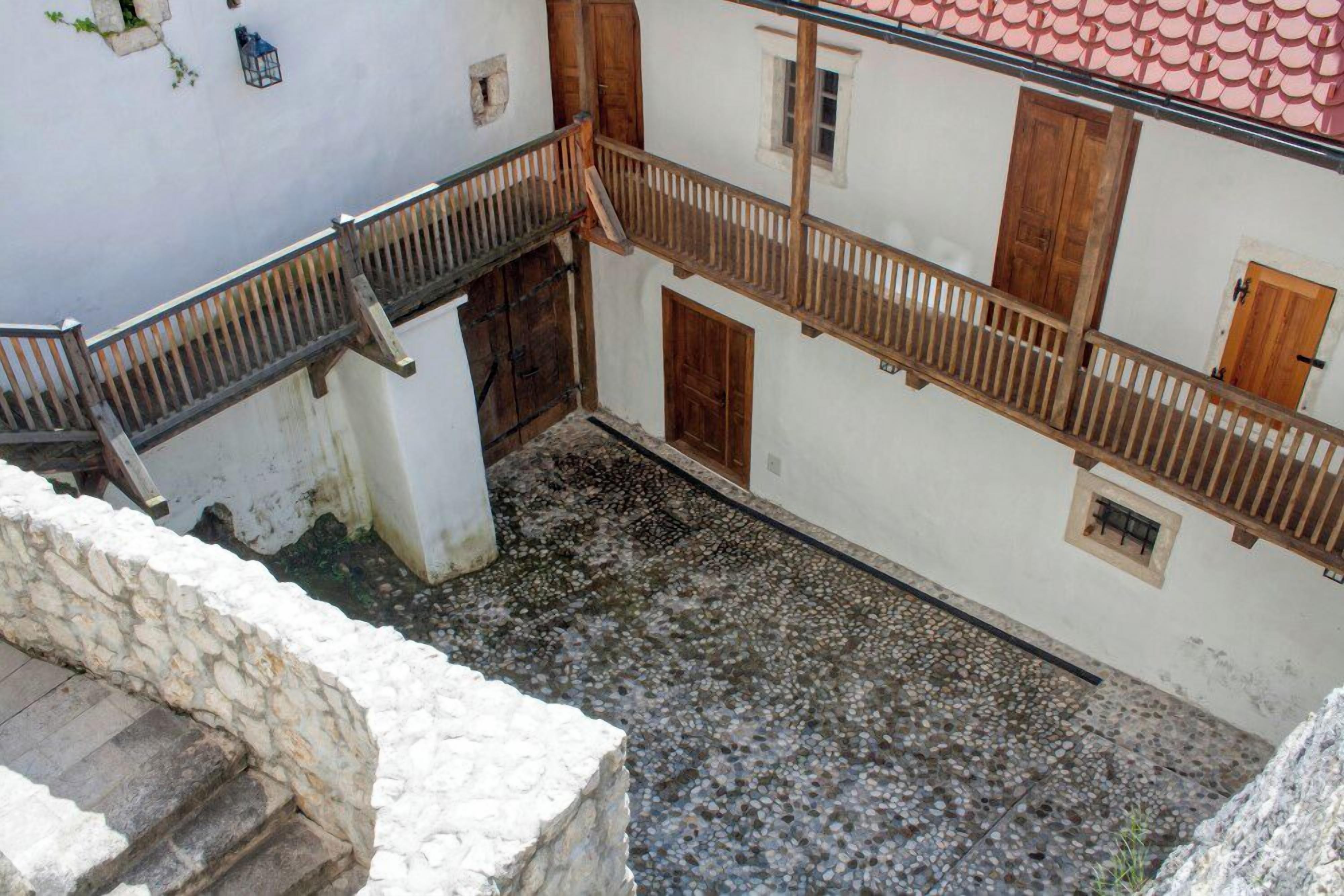 A courtyard with a stone floor, wooden railings, and a white building with a red-tiled roof.
