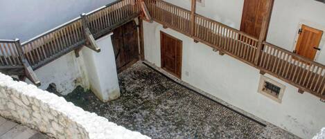 A courtyard with a stone floor, wooden railings, and a white building with a red-tiled roof.