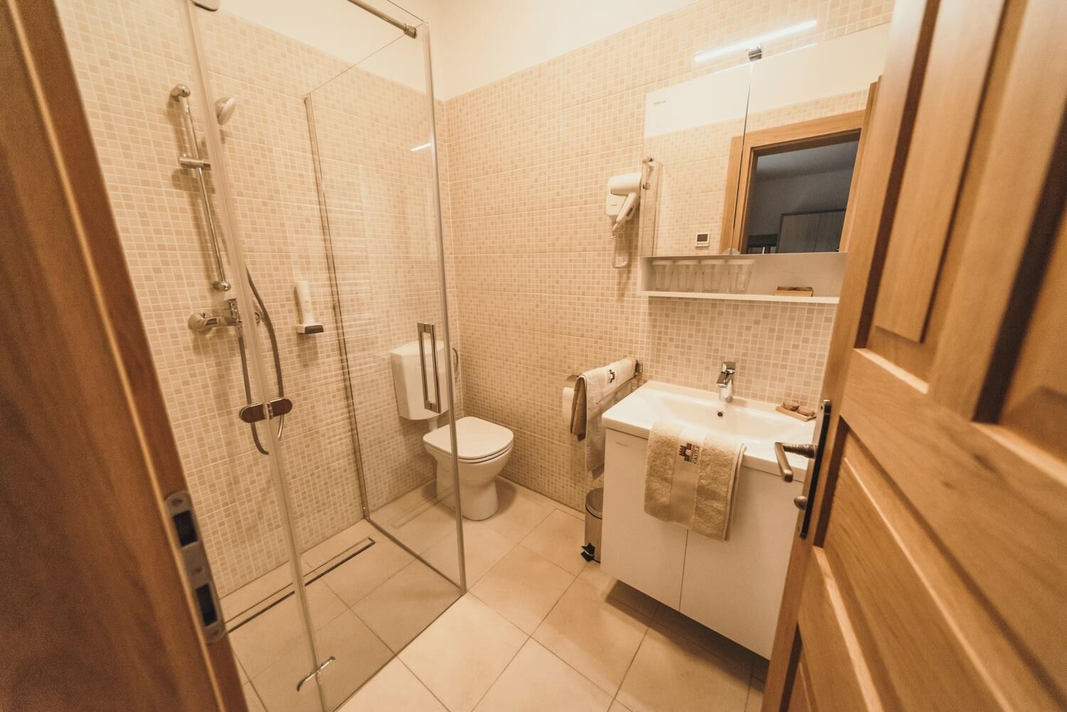 A modern bathroom with a glass-enclosed shower, a toilet, and a sink with a towel hanging on the side.