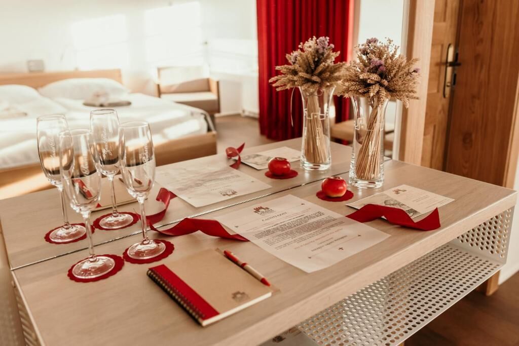 Una mesa de comedor bien ordenada con copas de vino, un bloc de notas y menús, con una cama y una cortina roja al fondo.