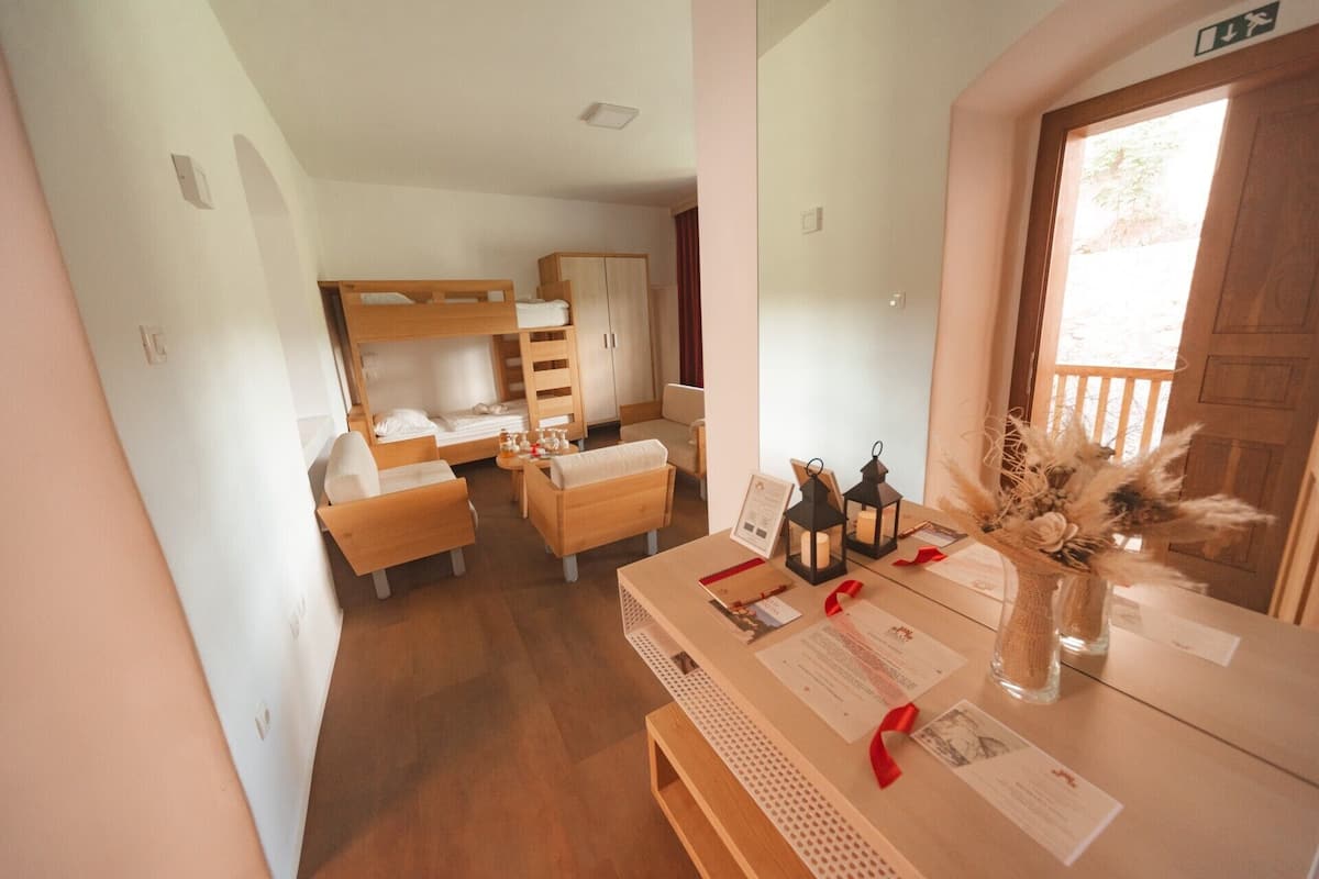 Una habitación acogedora con literas, un escritorio de madera con papeles y una mesita con un jarrón de flores secas.