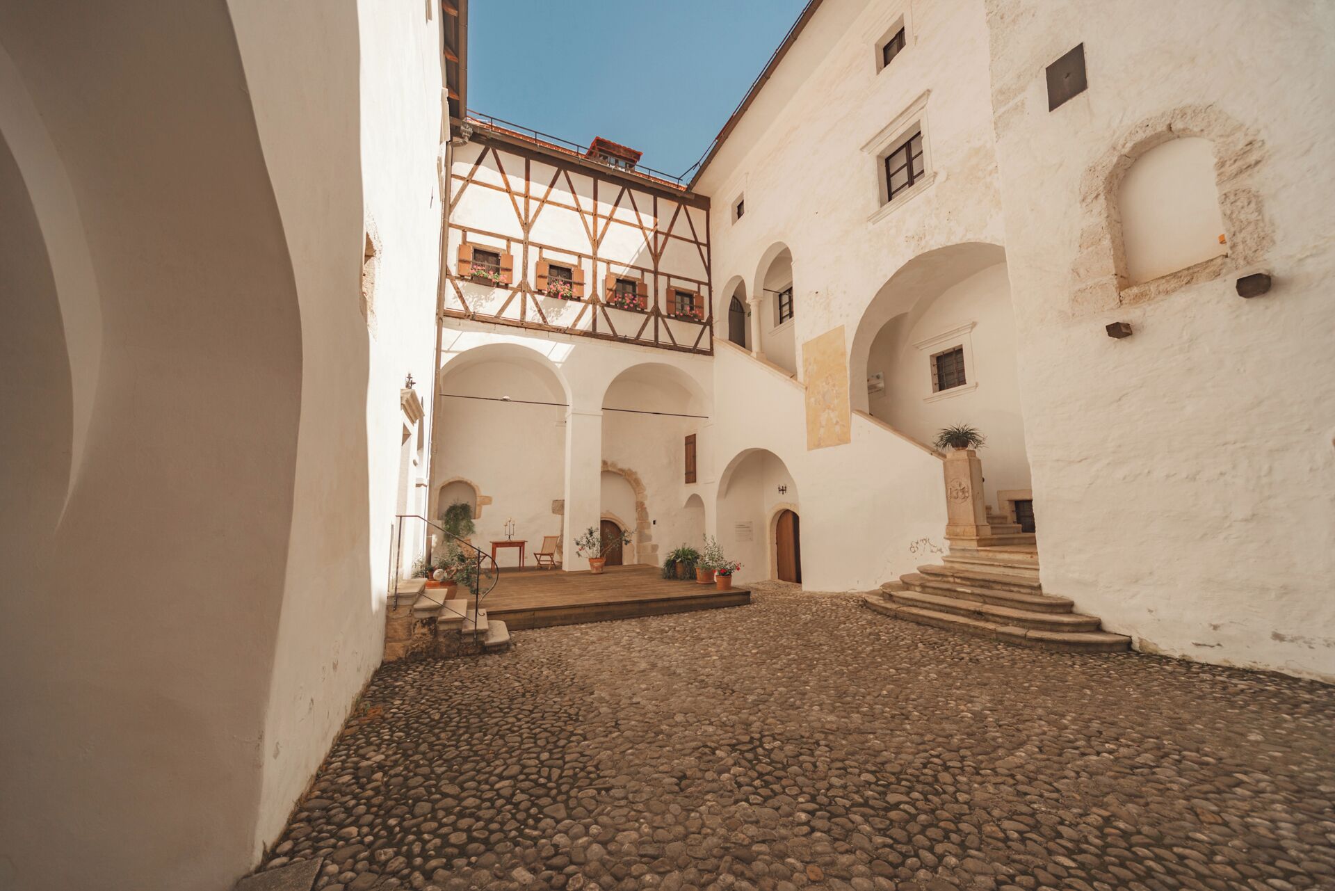 A courtyard with cobblestone flooring, white walls, and a wooden balcony.