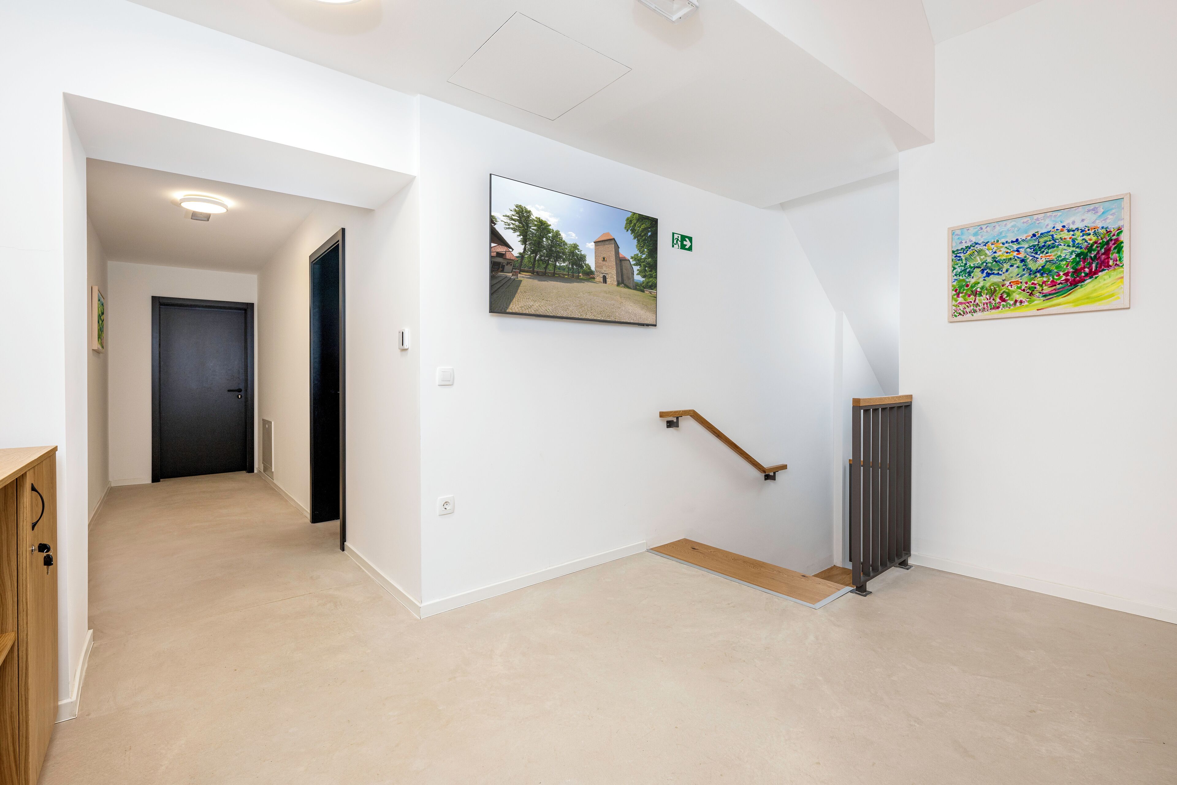 A hallway with a wooden cabinet, a black door, a ramp, and two framed pictures on the walls.