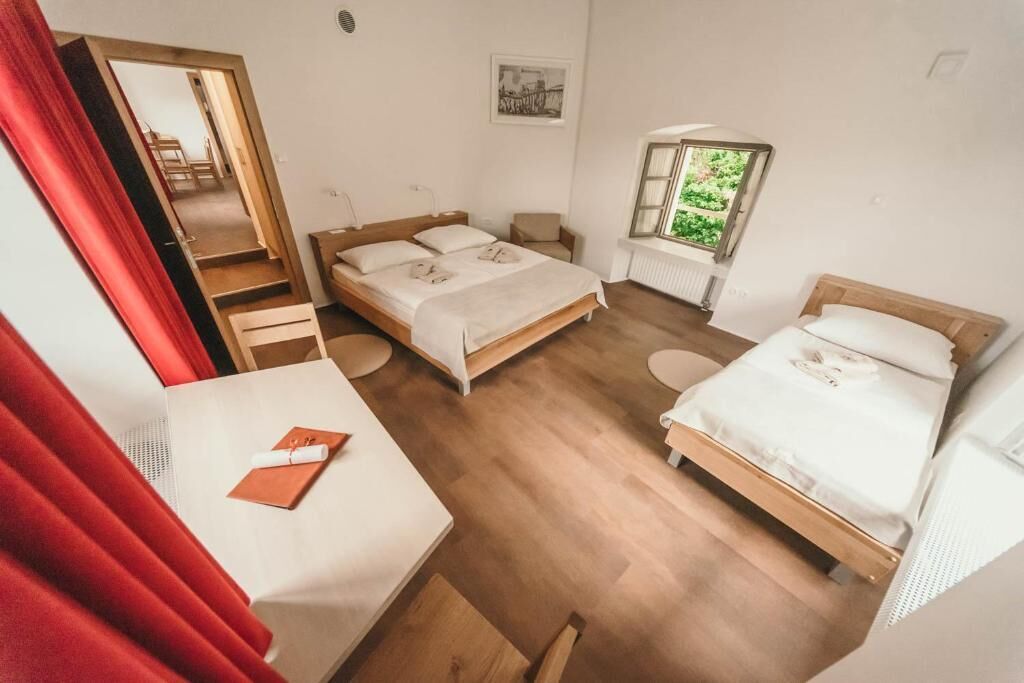 A room with two beds, a desk, a chair, a window with a view, and a mirror.