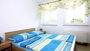 A single bed with a striped bedspread, a bedside table with a lamp, and a window with curtains.
