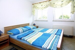 A single bed with a striped bedspread, a bedside table with a lamp, and a window with curtains. - Charmante Ferienwohnung auf Rügen, Altenkirchen (Altenkirchen)
