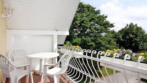 A balcony with white chairs and a table, a white railing, and a view of trees and flowers.