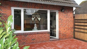 A brick house with a large window and a small porch area. - Doppelhaushälfte Friesenglück mit Sauna (Dornumersiel)