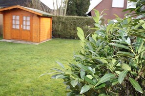A wooden shed with a door and windows, a well-maintained lawn, and a hedge in the background.