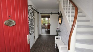 A hallway with a red door, a white staircase, and a dining area in the background. - Doppelhaushälfte Friesenglück mit Sauna (Dornumersiel)