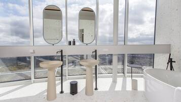 Un baño moderno con dos lavamanos, un espejo grande y una bañera independiente.