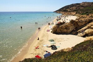 Ein Strand mit klarem Wasser, felsigem Gelände und Menschen, die sich sonnen.