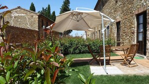 A stone building with a garden patio, outdoor seating, and a large umbrella. - Apartment in Campiglia Marittima (Campiglia Marittima)