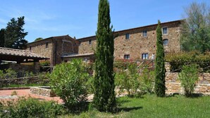A stone building with multiple windows and a courtyard with greenery. - Apartment in Campiglia Marittima (Campiglia Marittima)