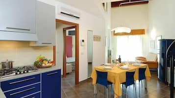 Une cuisine compacte équipée d’une cuisinière à gaz, de meubles bleus et d’un coin repas avec une nappe jaune et des chaises bleues.