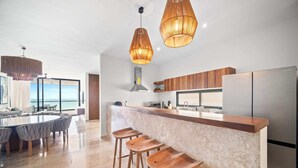 A modern kitchen with a central island, bar stools, and pendant lighting. - 4-Bedroom Beachfront Apartment (San Bruno)
