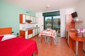 Quarto de hotel com cama, mesa de jantar com cadeiras, cozinha compacta, televisão e janela com vista.