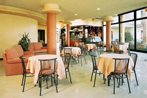 A hotel lobby with round tables and chairs, a sofa, and a bar area.