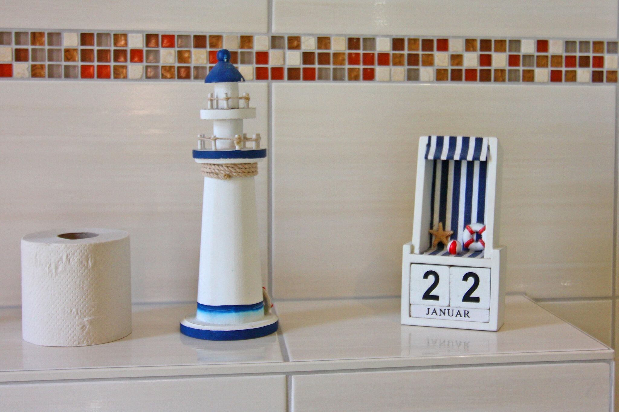 Une salle de bain avec des toilettes blanches, un phare décoratif et un calendrier indiquant la date du « 22 JANVIER ».
