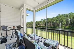 A covered outdoor area with wicker furniture and a view of a lake and forest. - Fall Deals + Snowbird Rates | Lake View, Pool, Close to the Beach (Santa Rosa Beach)