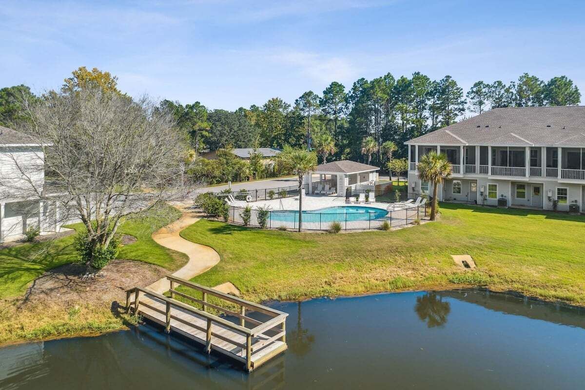 Una zona residencial con piscina, un puente de madera y una casa grande con balcón.