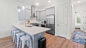 A modern kitchen with a central island, stainless steel appliances, and white cabinetry. - Fall Deals + Snowbird Rates | Lake View, Pool, Close to the Beach (Santa Rosa Beach)