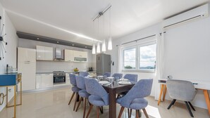 Eine moderne Küche mit weißen Schränken, einem Edelstahlkühlschrank und einem Essbereich mit einem dunklen Holztisch und blauen Stühlen.