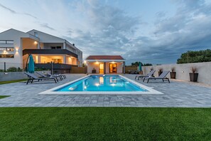 Una casa moderna con piscina, sillas de descanso y un césped cuidado.