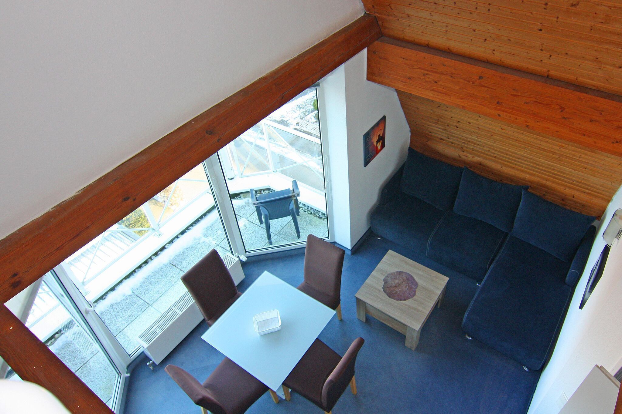 A room with a white table, four brown chairs, a blue sofa, and a wooden coffee table.