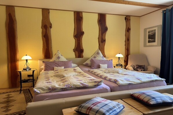 Une chambre double avec deux lits, chacun recouvert d’une couvre-lit à motifs floraux, deux tables de chevet avec des lampes, un mur décoratif en bois, une chaise et un petit tapis.