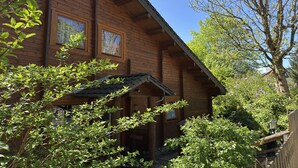 En stuga byggd av trä med ett sluttande tak, stora fönster och en inglasad veranda.
