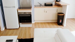 A compact kitchenette with a microwave, oven, and sink, a white sofa, and a small trash bin. - Appartement T2 55m2 Plein Centre St-brieuc (Saint-Brieuc)